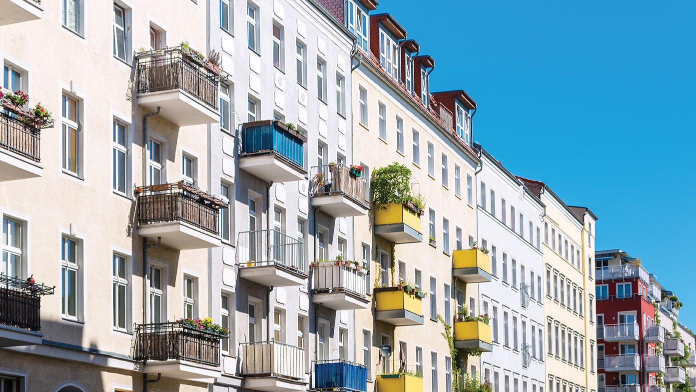 Das Bild zeigt eine geschlossene, städtische Altbau-Fassade mit Balkonen, die von den Bewohnern unterschiedlich ausgestattet wurden