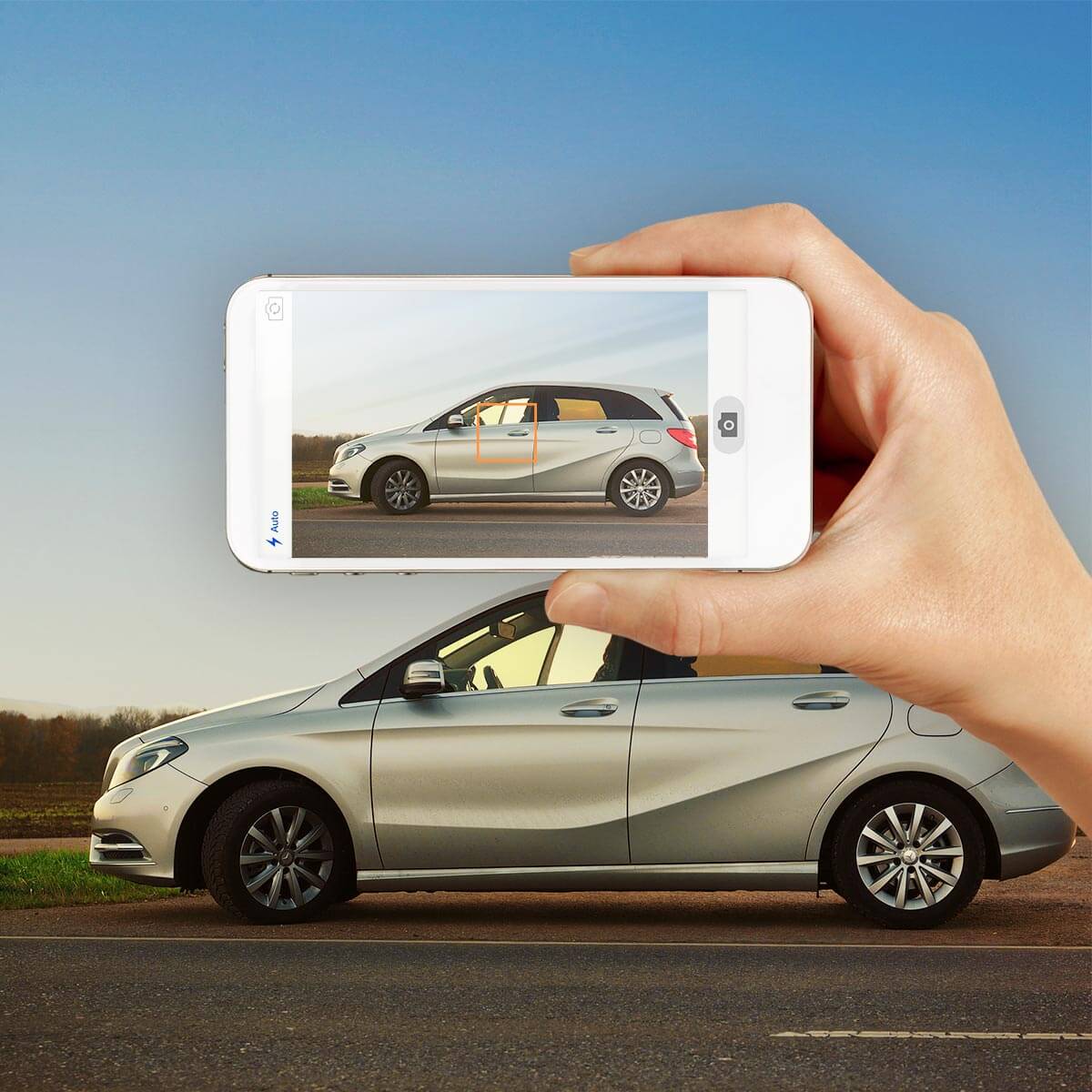 Das Bild zeigt einen neuen silbernen PKW im Hintergrund mit einer Smartphone-Kamera-App im Vordergrund, die gerade das Auto fotografiert.